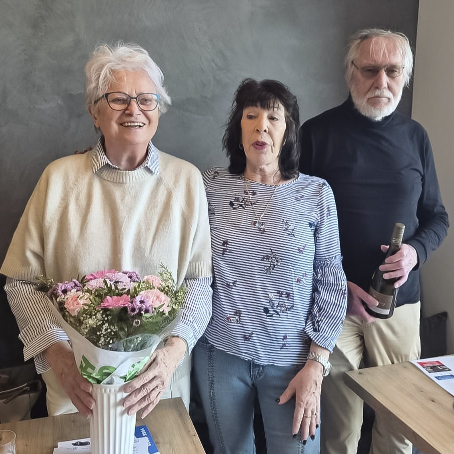 drei stehende Personen, eine mit Blumen