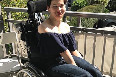 Frau im E-Rollstuhl auf einem Balkon