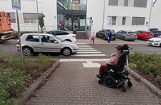 E-Rollstuhlfahrende vor einem Straßenübergang