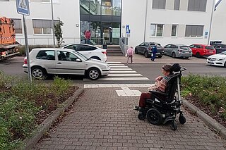 E-Rollstuhlfahrende vor einem Straßenübergang