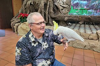 Rudi Bamberger mit einem papageienähnlichen Vogel auf dem Arm (Kakadu)