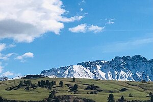 ein Panoramabild mit blauem Himmel, Wölkchen und einem schneebedeckten Berg im Hintergrund