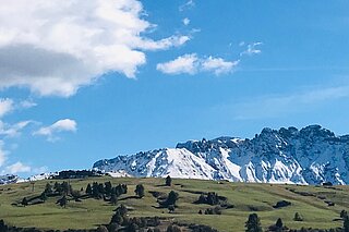ein Panoramabild mit blauem Himmel, Wölkchen und einem schneebedeckten Berg im Hintergrund