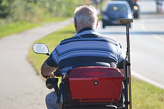 Mann von hinten auf einem E-Scooter, fährt eine Straße lang