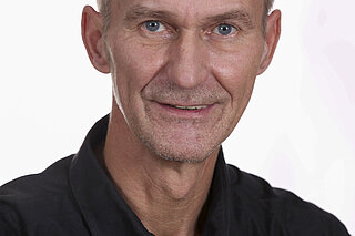 Man sieht einen drahtigen Mann Anfang 60. Er trägt ein schwarzes Hemd und lächelt sympathisch in die Kamera. Es ist Peter Reichert, der nun als BSK-Pressesprecher in den Ruhestand geht.