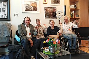 Vier Menschen sitzen vor einer bebilderten Wand