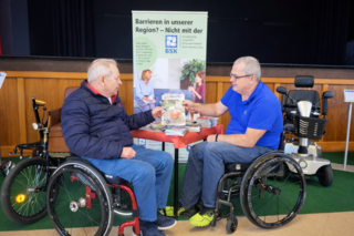 Zwei Rollstuhlfahrer vor Rudis Informationsstand