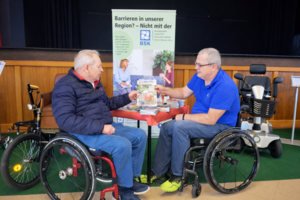 Zwei Rollstuhlfahrer vor Rudis Informationsstand