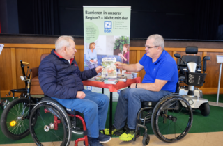 Zwei Rollstuhlfahrer vor Rudis Informationsstand