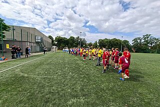 Manschaften in Aufstellung (Reihe, seitlich) auf Rasen mit blauem Himmel und Schönwetterwölkchen