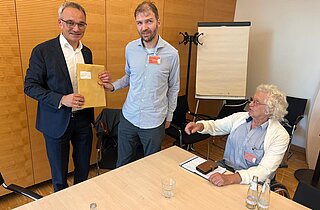 Drei Männer, Jörg übergibt die Unterschriften an Herrn Oellers