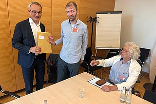 Drei Männer, Jörg übergibt die Unterschriften an Herrn Oellers