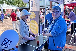 Ein Mensch hinter und ein Mensch vorm BSK-Stand, vorn im Bild ein BSK-Luftballon