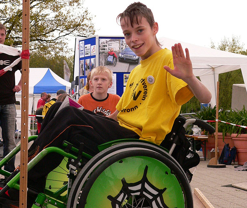 Junge mit gelbem T-Shirt im Rollstuhl.