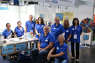 Das Foto zweigt neun Personen in blauen BSK-Shirts an einem Messestand. Es handelt sich um das Team aus Haupt- udn Ehrenamtlichen des Bundesverbands, das vier Tage auf der RehaCare-Messe in Düsseldorf im Einsatz war.