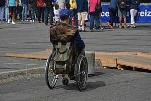 Rollstuhlfahrer von hinten mit Rucksack am Rolli auf einer Demo